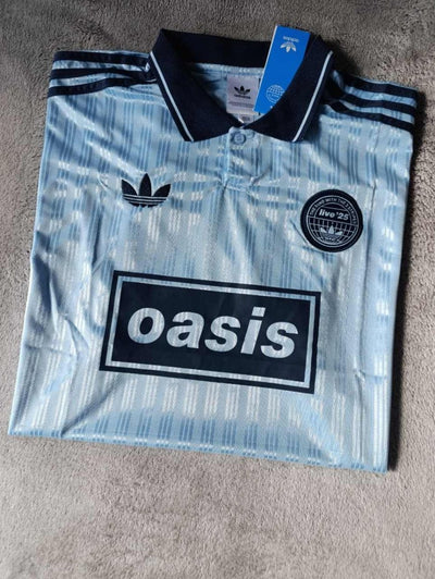 Vista lateral de la camiseta celeste Oasis x Adidas mostrando la caída de la tela
