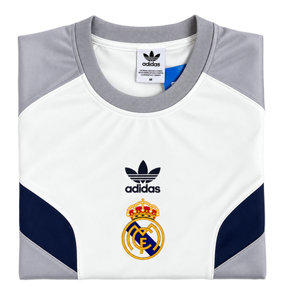 Camiseta retro del Real Madrid doblada, con el escudo dorado y el trébol de la marca en negro sobre el pecho