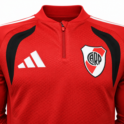 Detalle del pecho del fleece rojo de River Plate, con las tres barras de Adidas en blanco