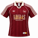 Camiseta Adidas World Wide vinotinto con cuello polo, el trébol y ADIDAS en letras grandes al pecho