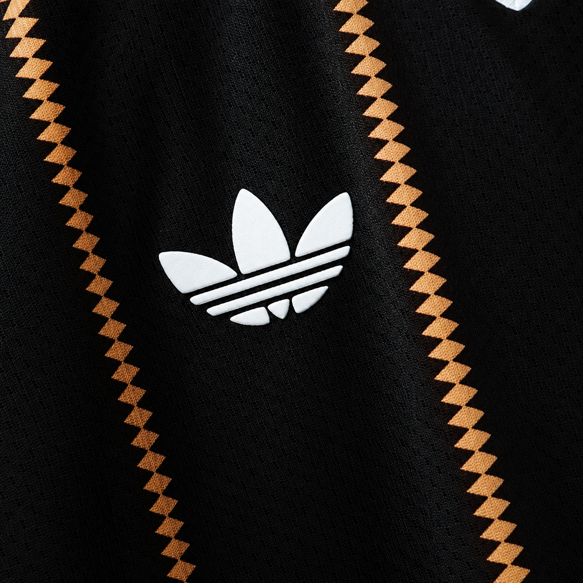 Detalle del trébol blanco sobre la tela negra de la camiseta de Alemania tercera 2026, entre las rayas de rombos dorados