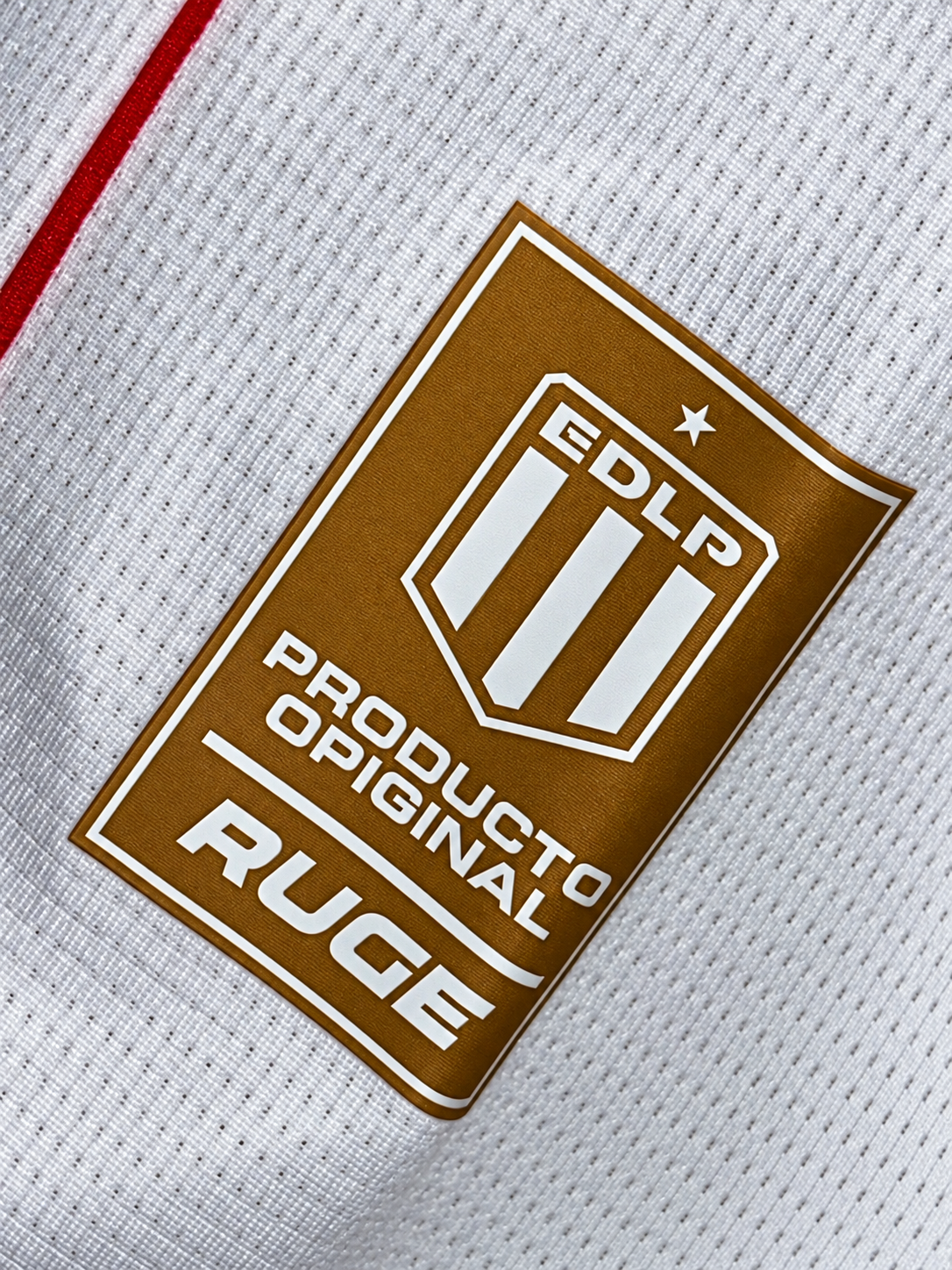 Etiqueta dourada EDLP da Ruge na parte de baixo da camisa branca do Estudiantes