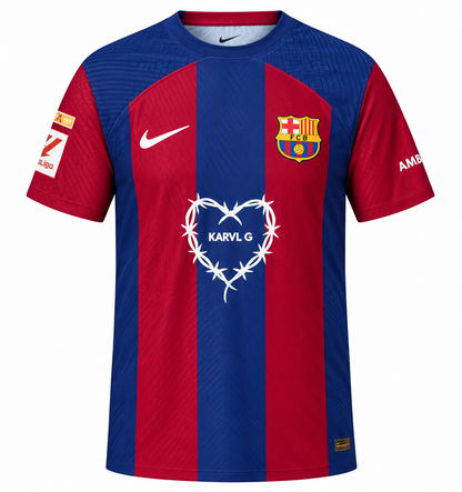 Frente de la camiseta del FC Barcelona x Karol G edición limitada, con rayas azul y grana, corazón de alambre de púas blanco con KARVL G al pecho, Nike blanco y parche de La Liga