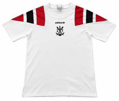 Frente de la camiseta blanca del Flamengo con hombros rojo y negro, trébol de Adidas y el emblema del ancla con CRF