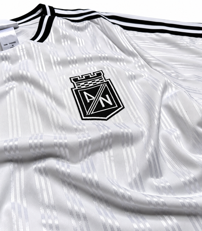 Detalhe do escudo preto da camisa Icon do Atlético Nacional sobre o tecido branco de listras finas
