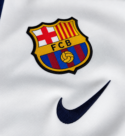 Escudo del FC Barcelona termosellado sobre la camiseta retro blanca, con el logo de la marca en azul oscuro al lado