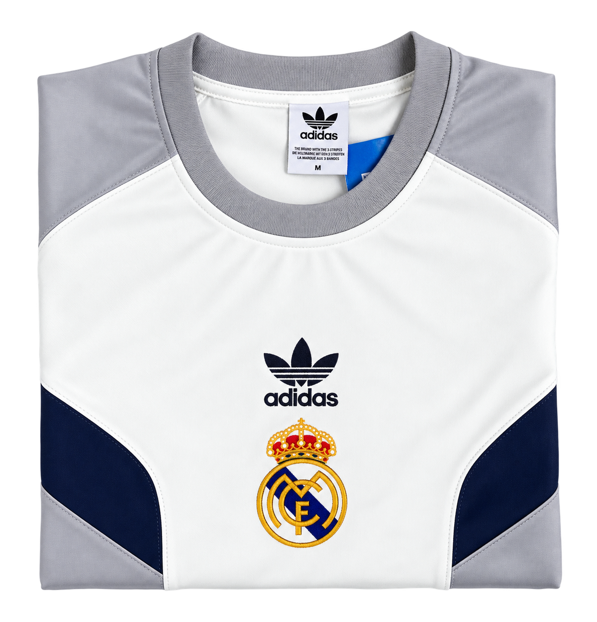 Camiseta retro del Real Madrid doblada, con el escudo dorado y el trébol de la marca en negro sobre el pecho