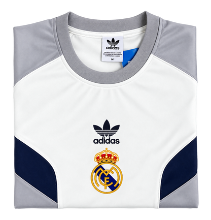 Camiseta retro del Real Madrid doblada, con el escudo dorado y el trébol de la marca en negro sobre el pecho